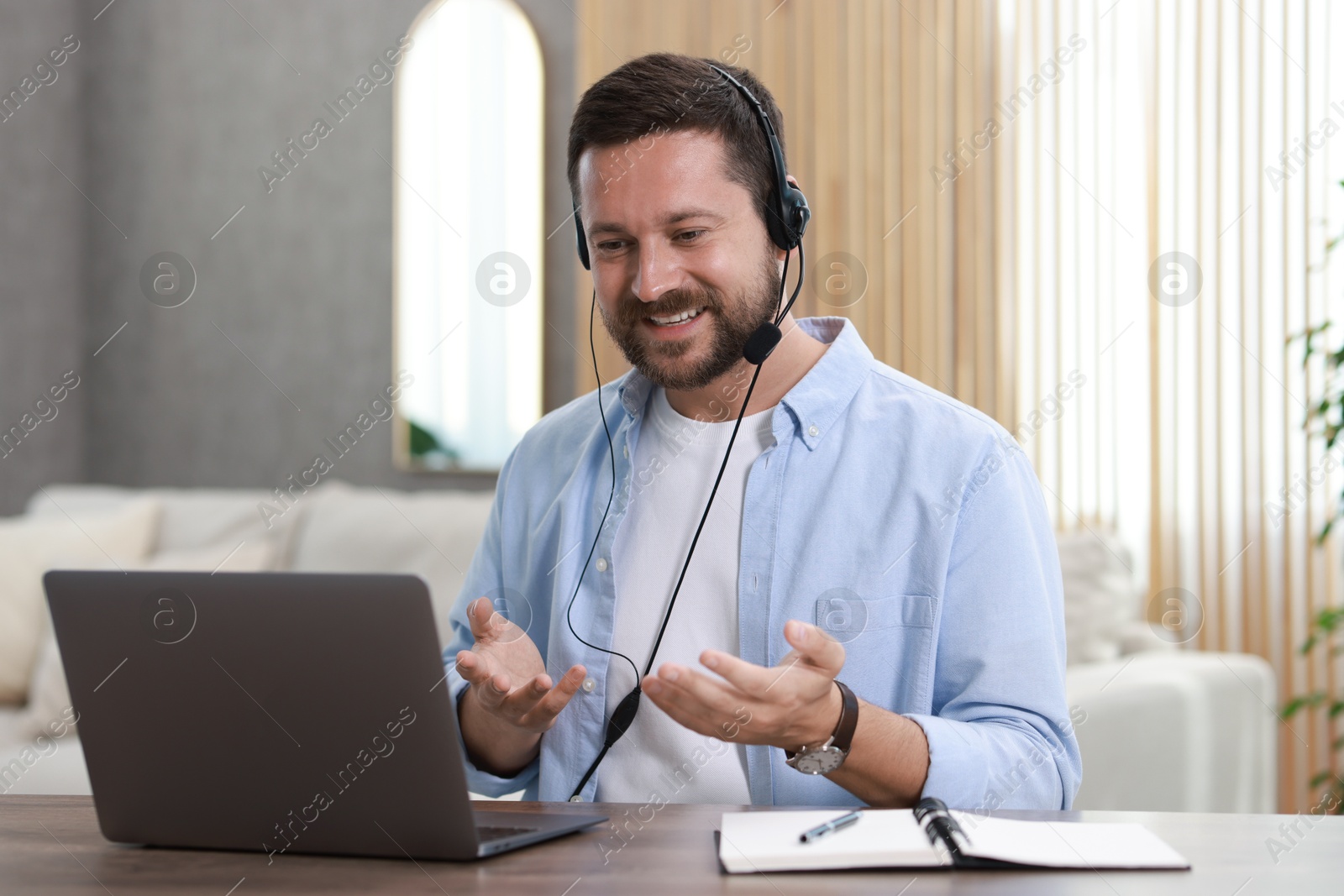 Photo of Interpreter in headset having video chat via laptop at wooden table indoors