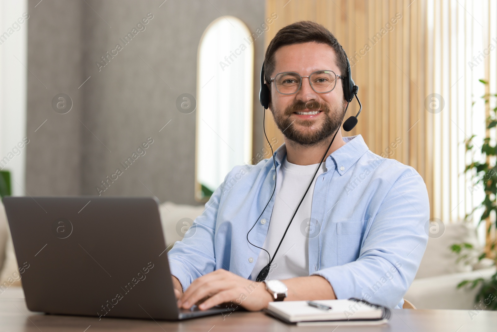 Photo of Interpreter in headset having video chat via laptop at wooden table indoors