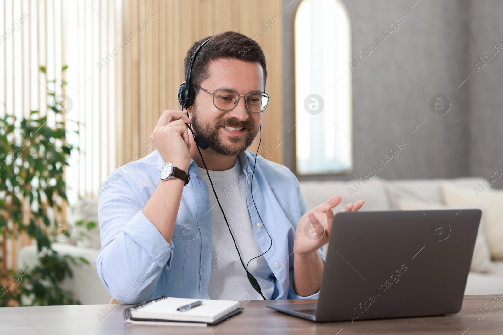 Photo of Interpreter in headset having video chat via laptop at wooden table indoors