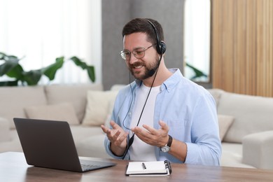 Interpreter in headset having video chat via laptop at wooden table indoors