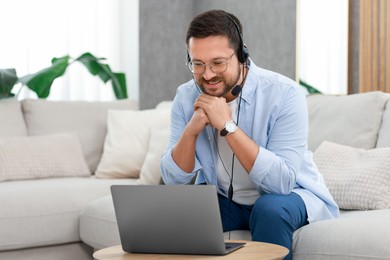 Interpreter in headset having video chat via laptop at wooden table indoors