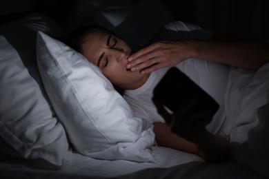 Photo of Bad habit. Young woman using smartphone in bed at night