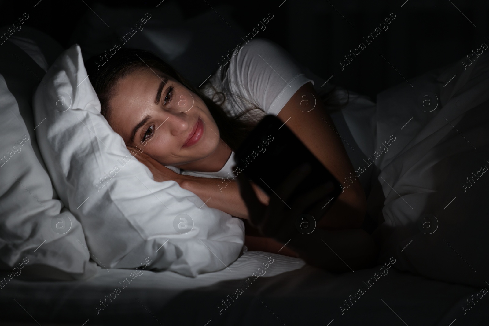 Photo of Bad habit. Young woman using smartphone in bed at night