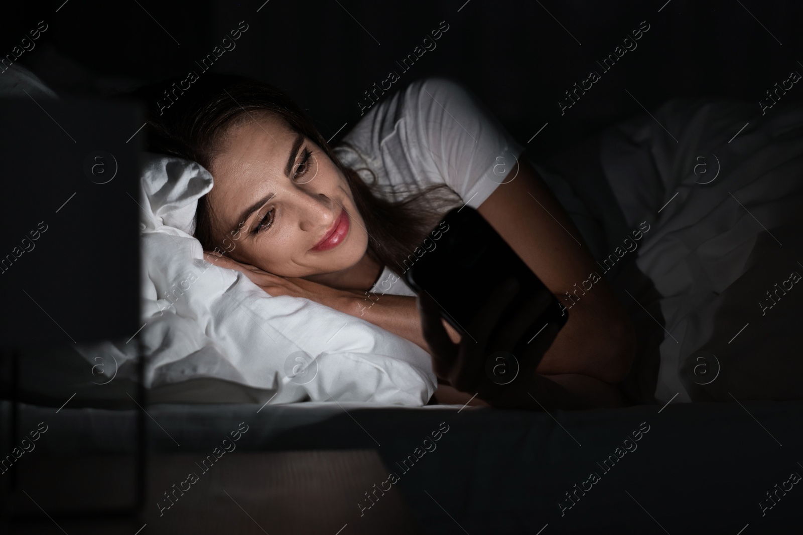 Photo of Bad habit. Young woman using smartphone in bed at night