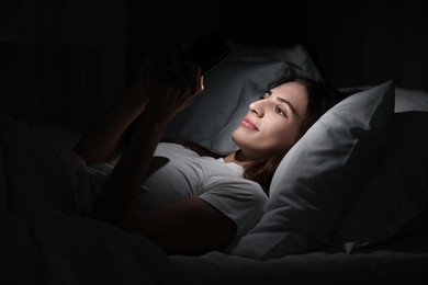 Photo of Bad habit. Young woman using smartphone in bed at night