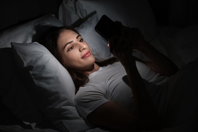 Photo of Bad habit. Young woman using smartphone in bed at night