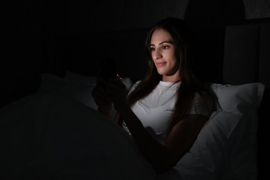 Photo of Bad habit. Young woman using smartphone in bed at night