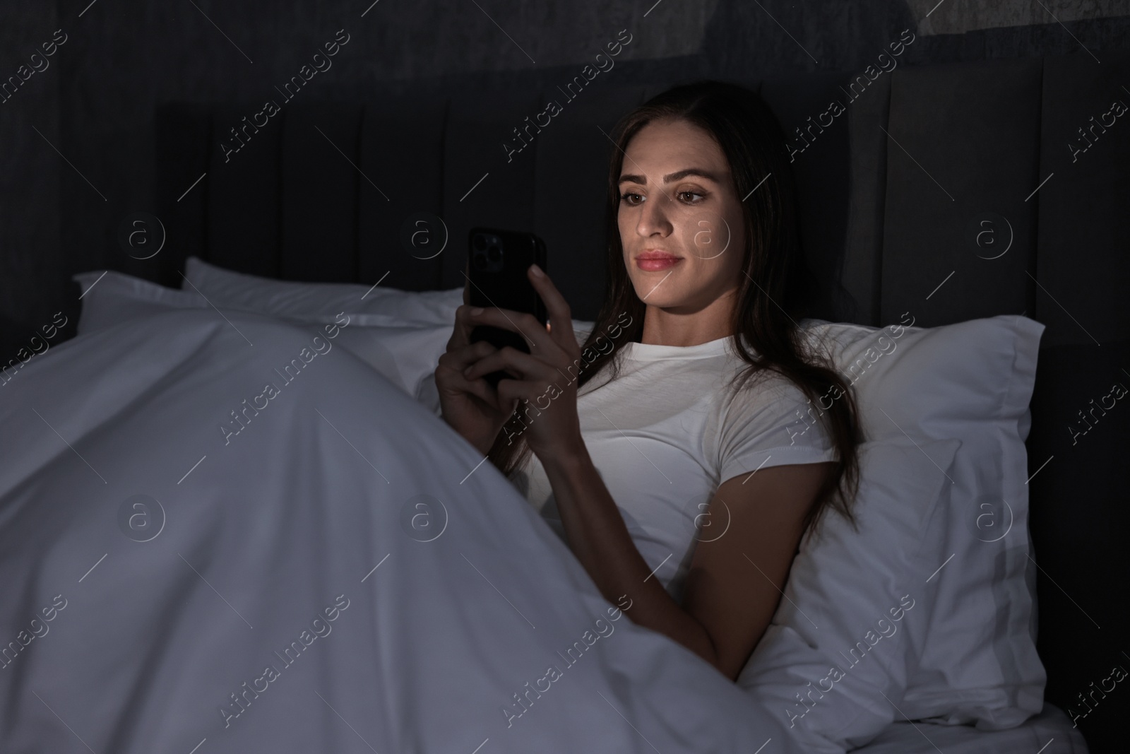 Photo of Bad habit. Young woman using smartphone in bed at night