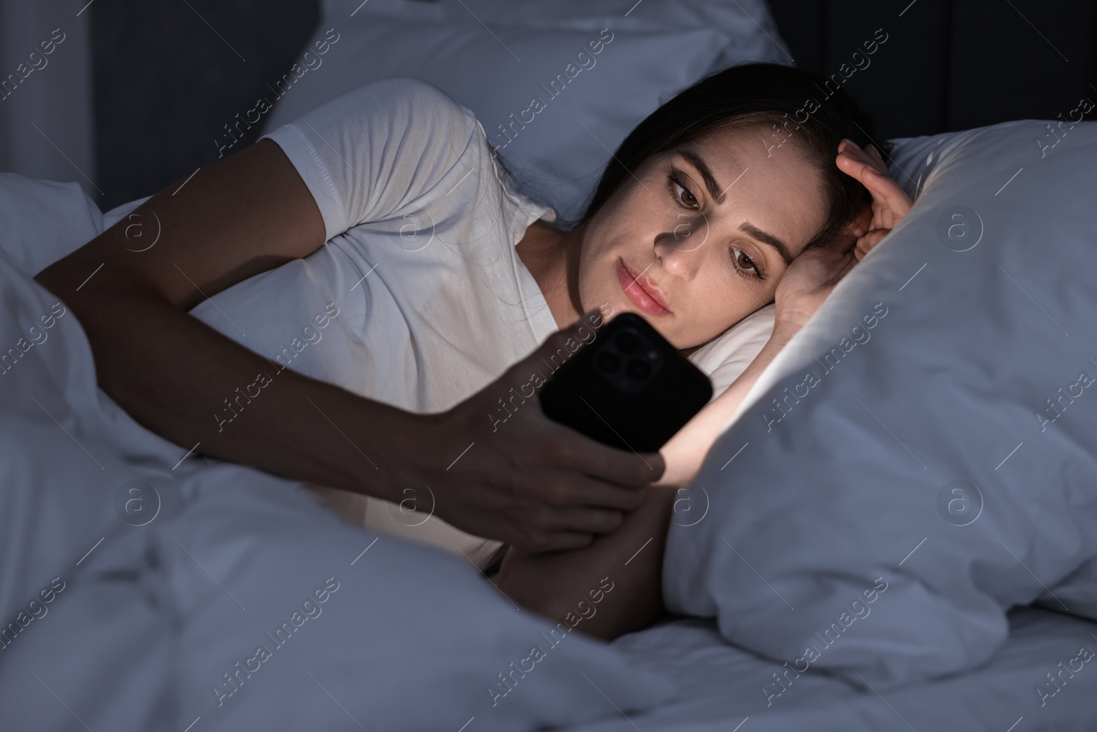 Photo of Bad habit. Young woman using smartphone in bed at night