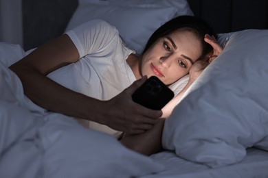 Photo of Bad habit. Young woman using smartphone in bed at night