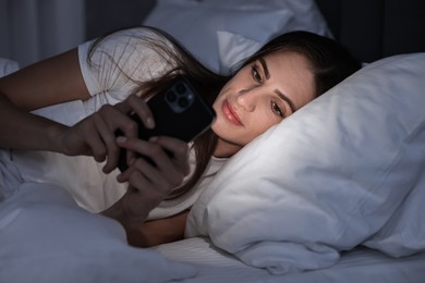 Photo of Bad habit. Young woman using smartphone in bed at night