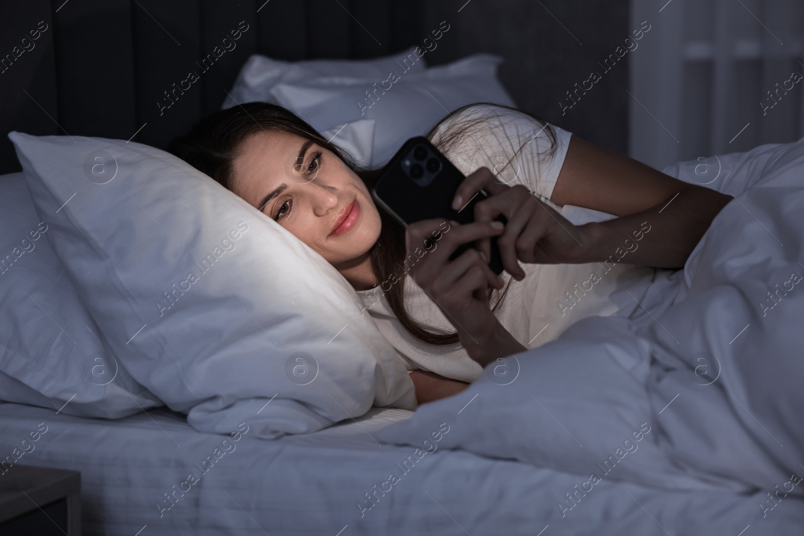 Photo of Bad habit. Young woman using smartphone in bed at night