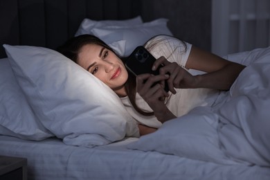 Photo of Bad habit. Young woman using smartphone in bed at night