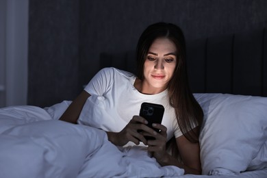 Photo of Bad habit. Young woman using smartphone in bed at night