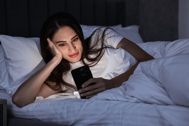 Photo of Bad habit. Young woman using smartphone in bed at night