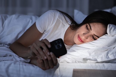 Photo of Bad habit. Young woman using smartphone in bed at night