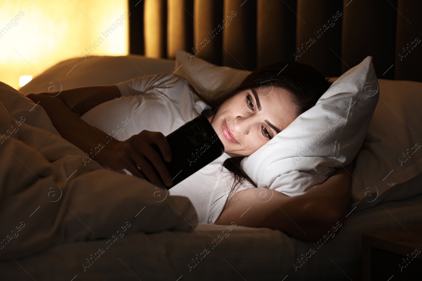 Photo of Bad habit. Young woman using smartphone in bed at night