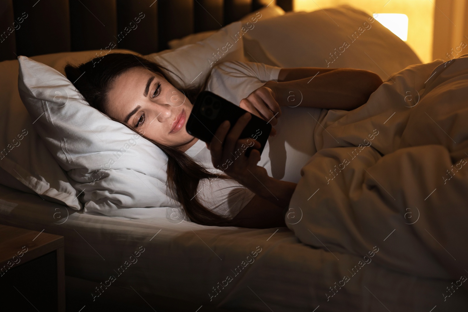 Photo of Bad habit. Young woman using smartphone in bed at night