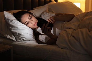 Photo of Bad habit. Young woman using smartphone in bed at night