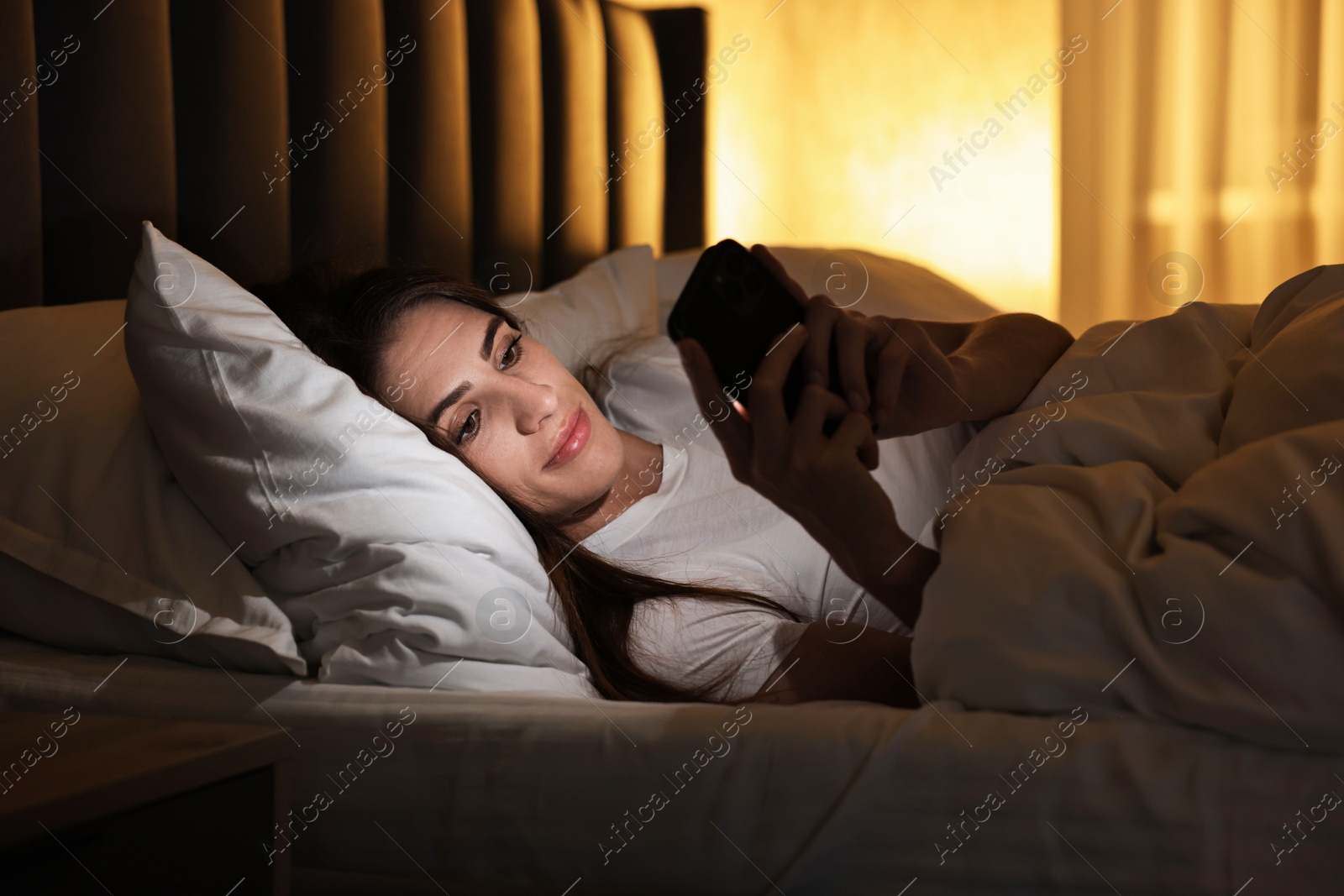 Photo of Bad habit. Young woman using smartphone in bed at night