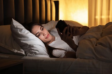 Photo of Bad habit. Young woman using smartphone in bed at night