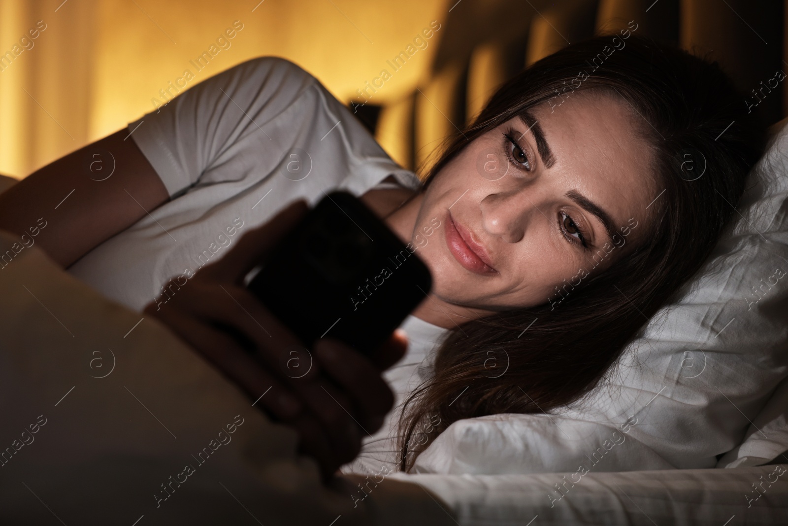 Photo of Bad habit. Young woman using smartphone in bed at night