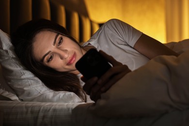 Photo of Bad habit. Young woman using smartphone in bed at night