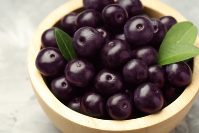 Photo of Ripe acai berries and leaves in bowl on table, closeup