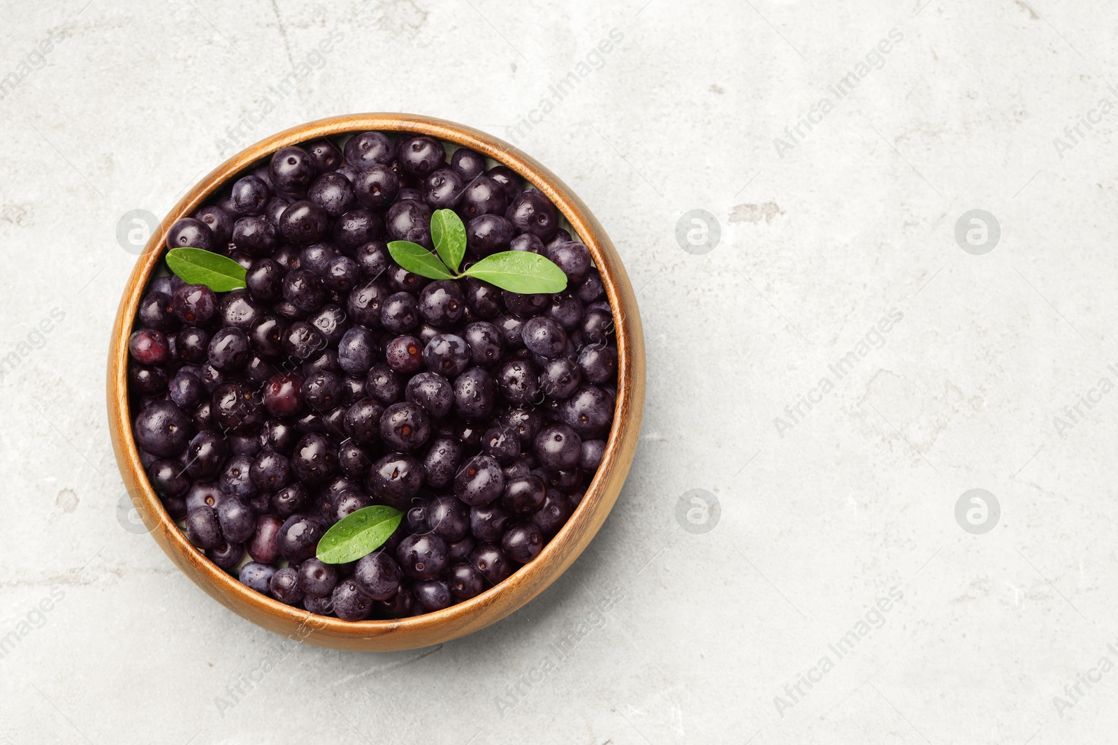 Photo of Ripe acai berries and leaves in bowl on light table, top view. Space for text