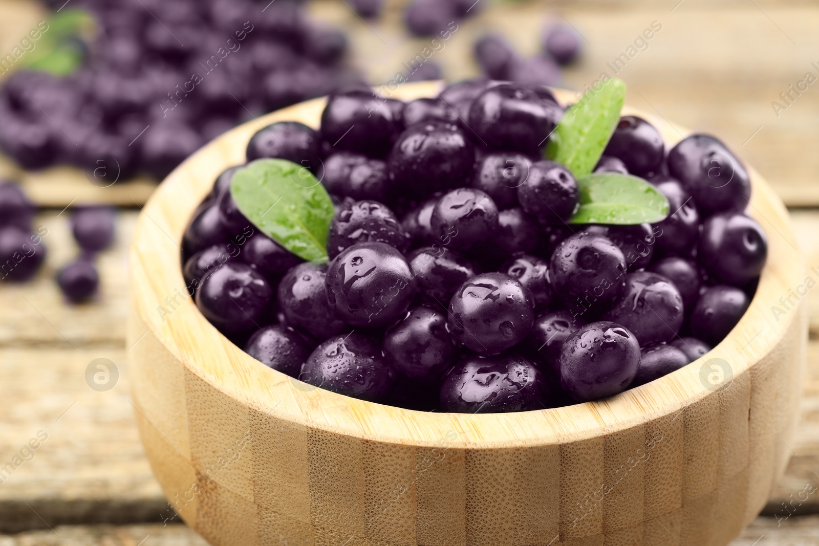 Photo of Ripe acai berries and leaves in bowl on wooden table, closeup