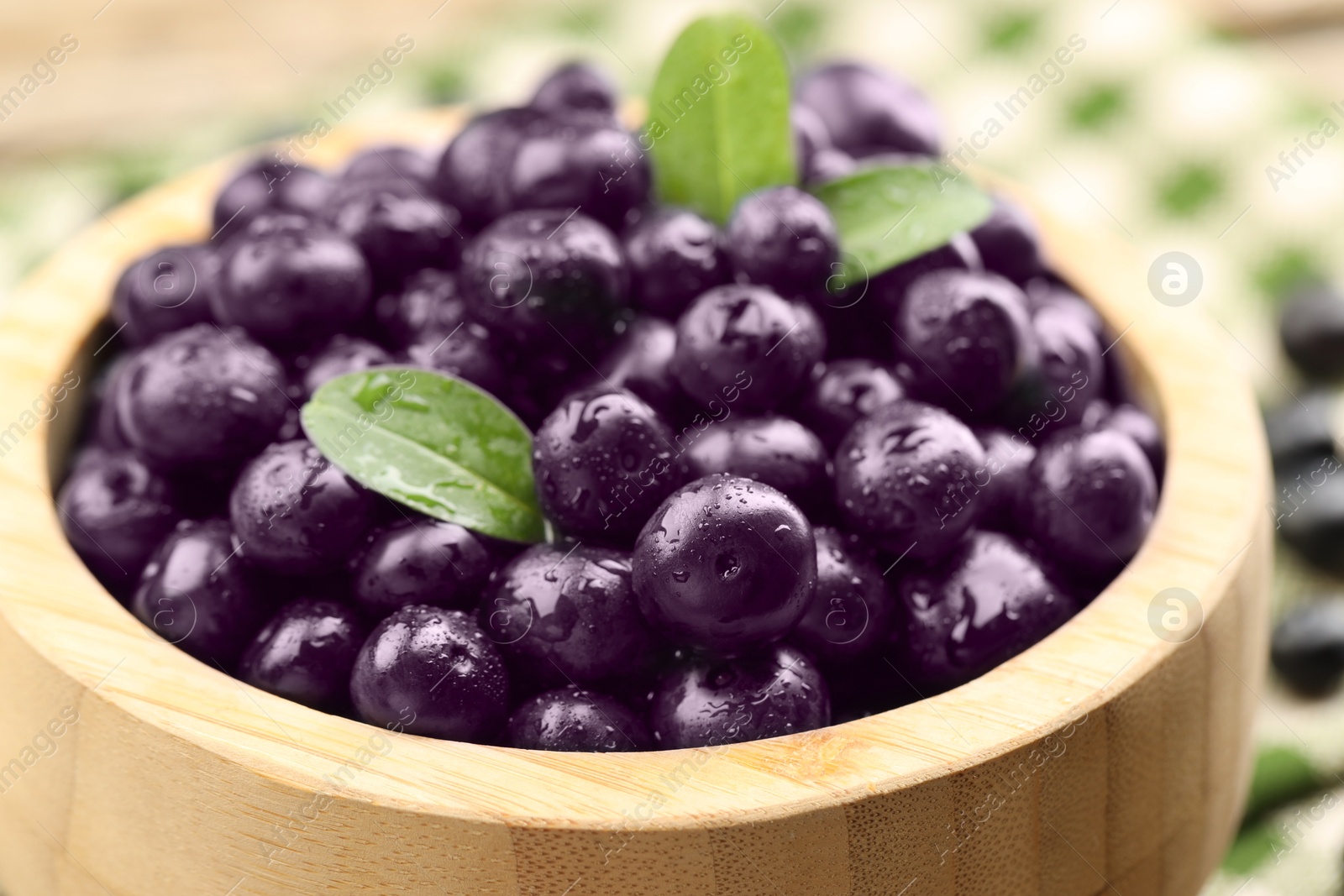 Photo of Ripe acai berries and leaves in bowl, closeup