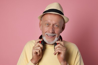 Portrait of handsome senior man with headphones on pink background