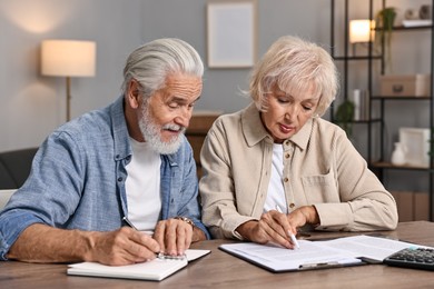 Photo of Pension savings. Senior couple planning budget at wooden table indoors