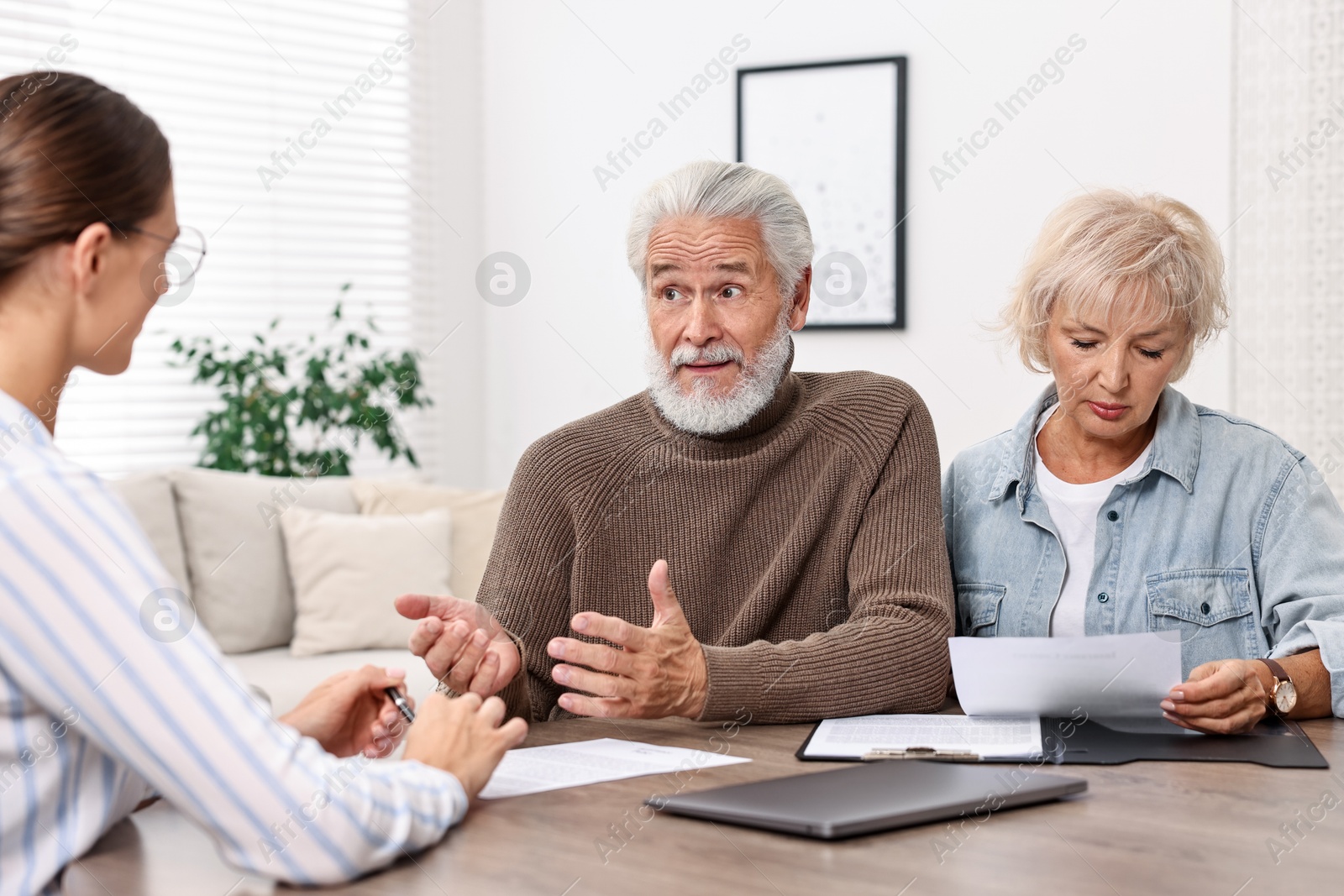 Photo of Pension plan. Senior couple consulting with insurance agent at wooden table indoors