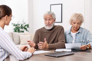 Photo of Pension plan. Senior couple consulting with insurance agent at wooden table indoors