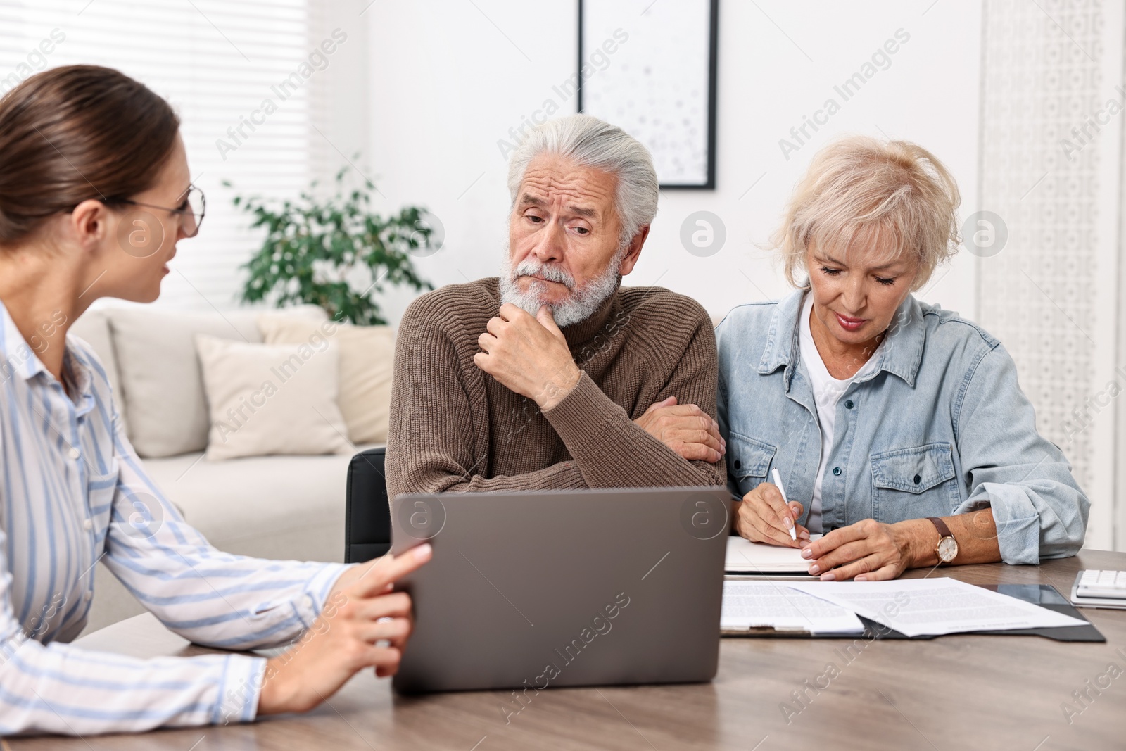 Photo of Pension plan. Senior couple consulting with insurance agent at wooden table indoors