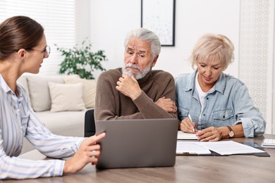 Photo of Pension plan. Senior couple consulting with insurance agent at wooden table indoors