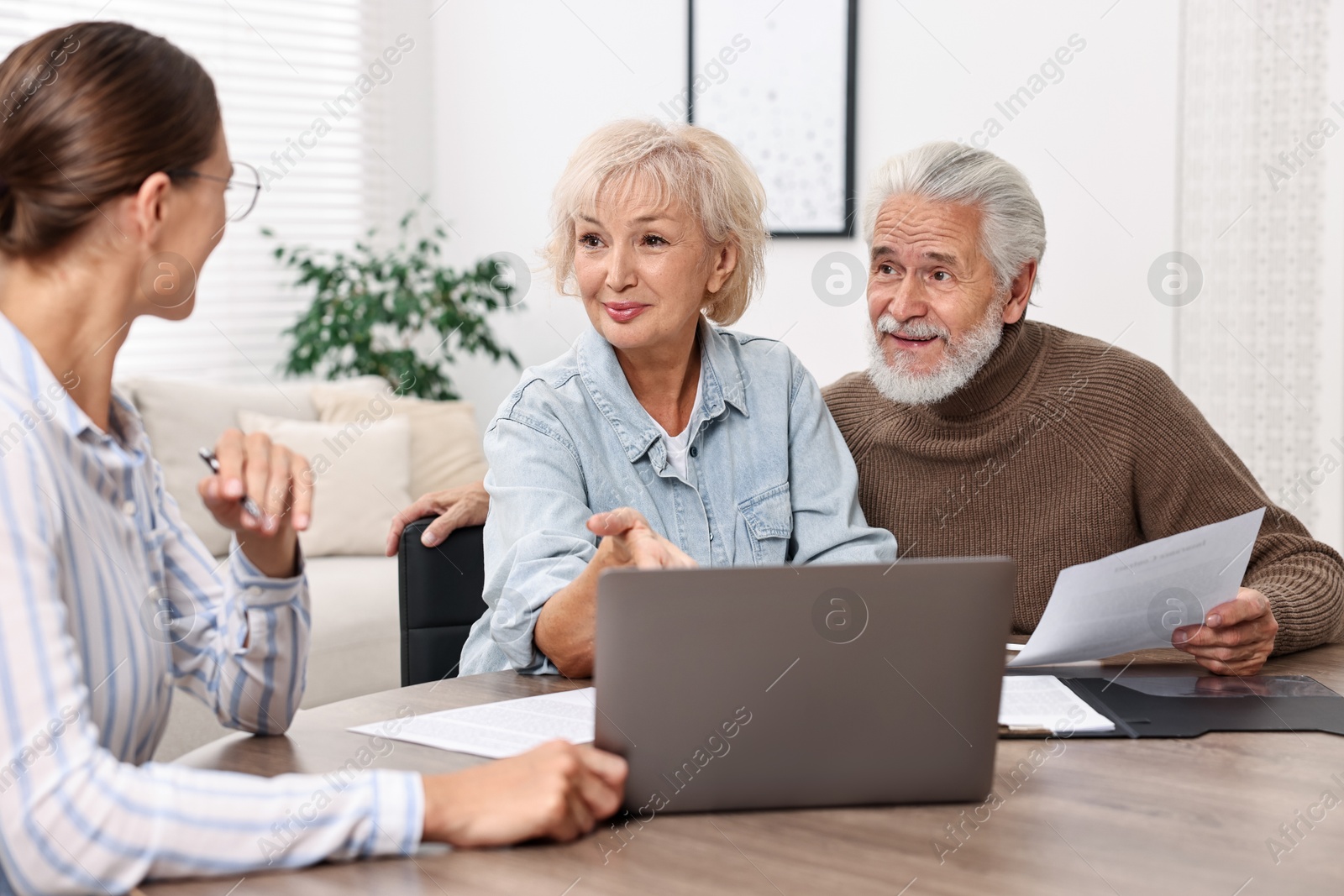 Photo of Pension plan. Senior couple consulting with insurance agent at wooden table indoors