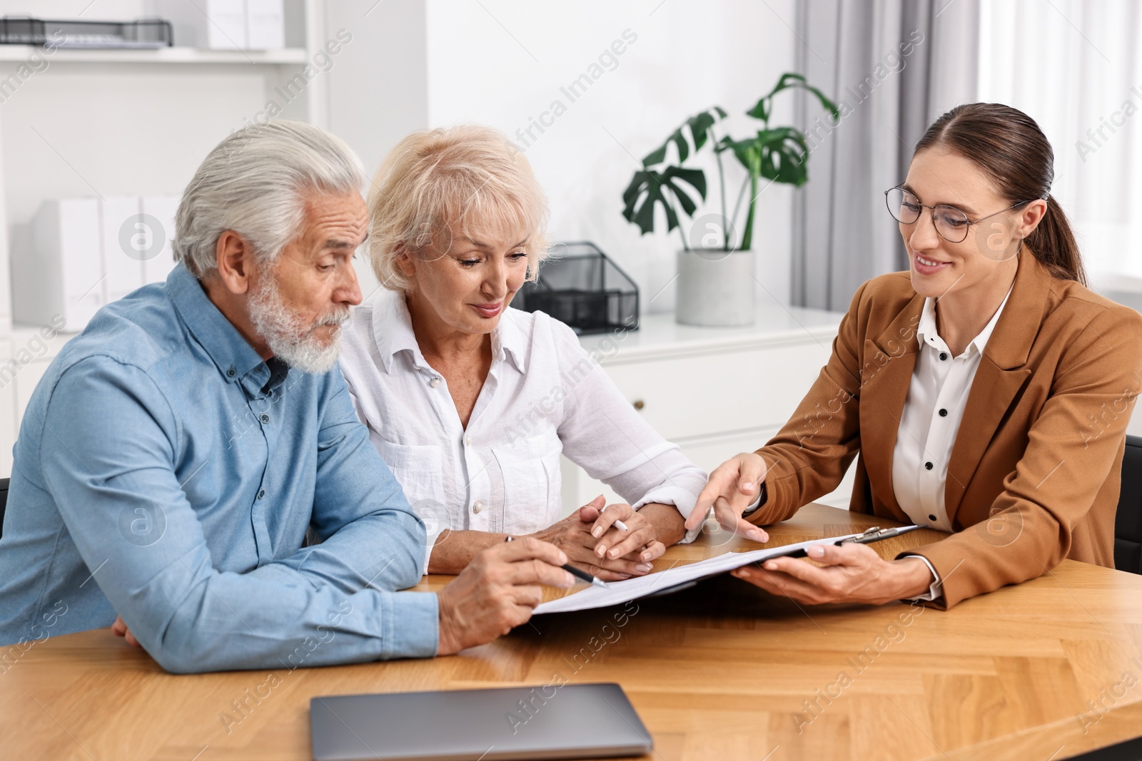 Photo of Pension plan. Senior couple consulting with insurance agent at wooden table indoors