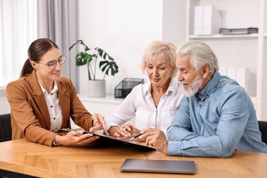 Photo of Pension plan. Senior couple consulting with insurance agent at wooden table indoors