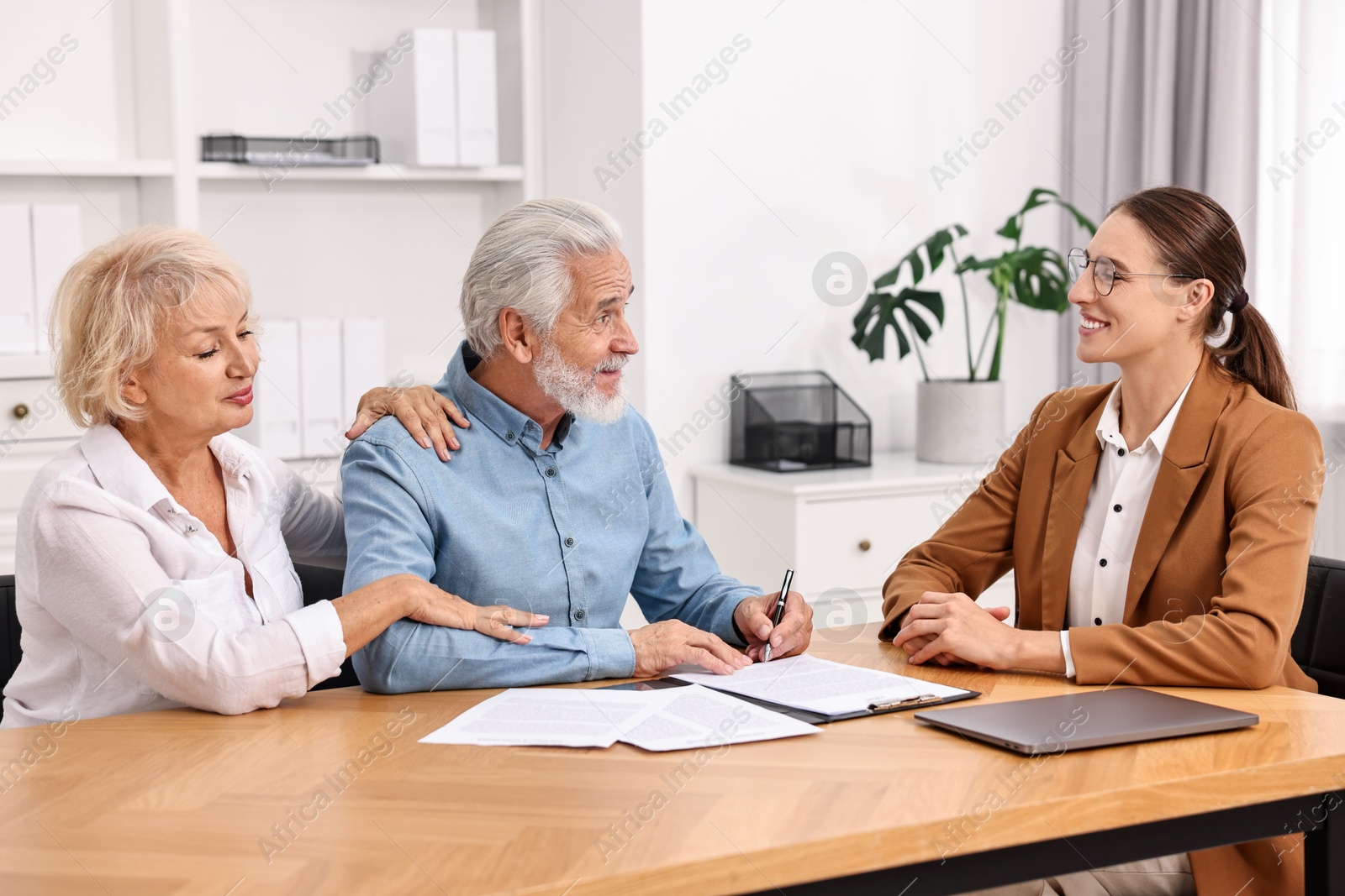 Photo of Pension plan. Senior couple consulting with insurance agent at wooden table indoors