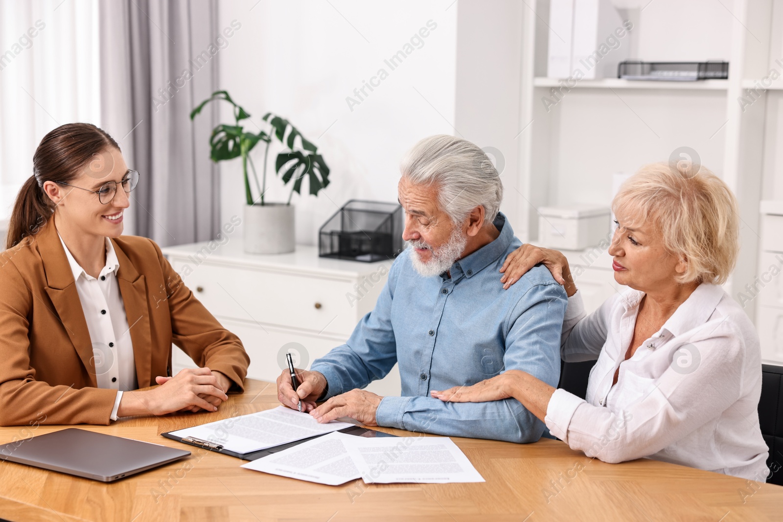 Photo of Pension plan. Senior couple consulting with insurance agent at wooden table indoors