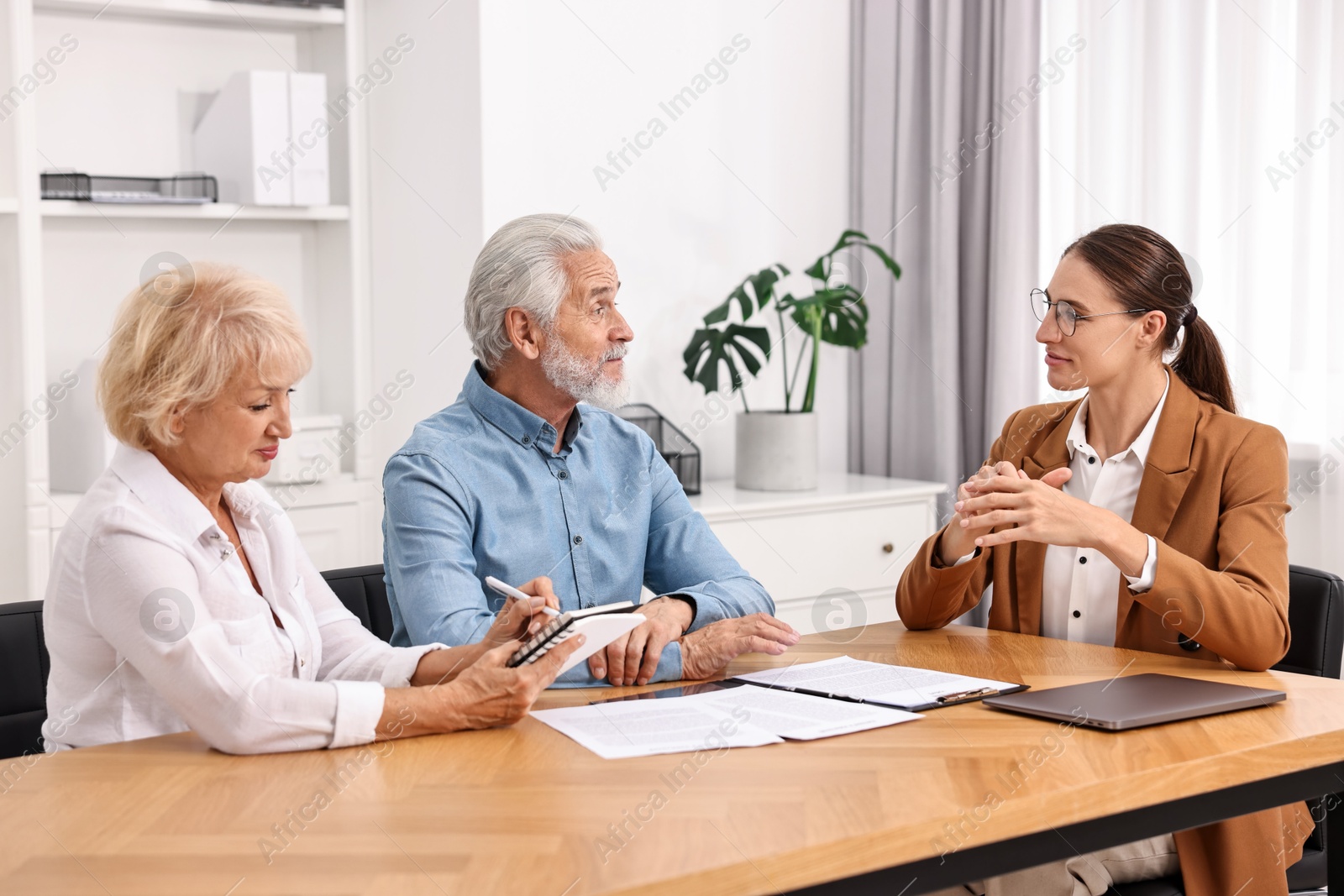 Photo of Pension plan. Senior couple consulting with insurance agent at wooden table indoors