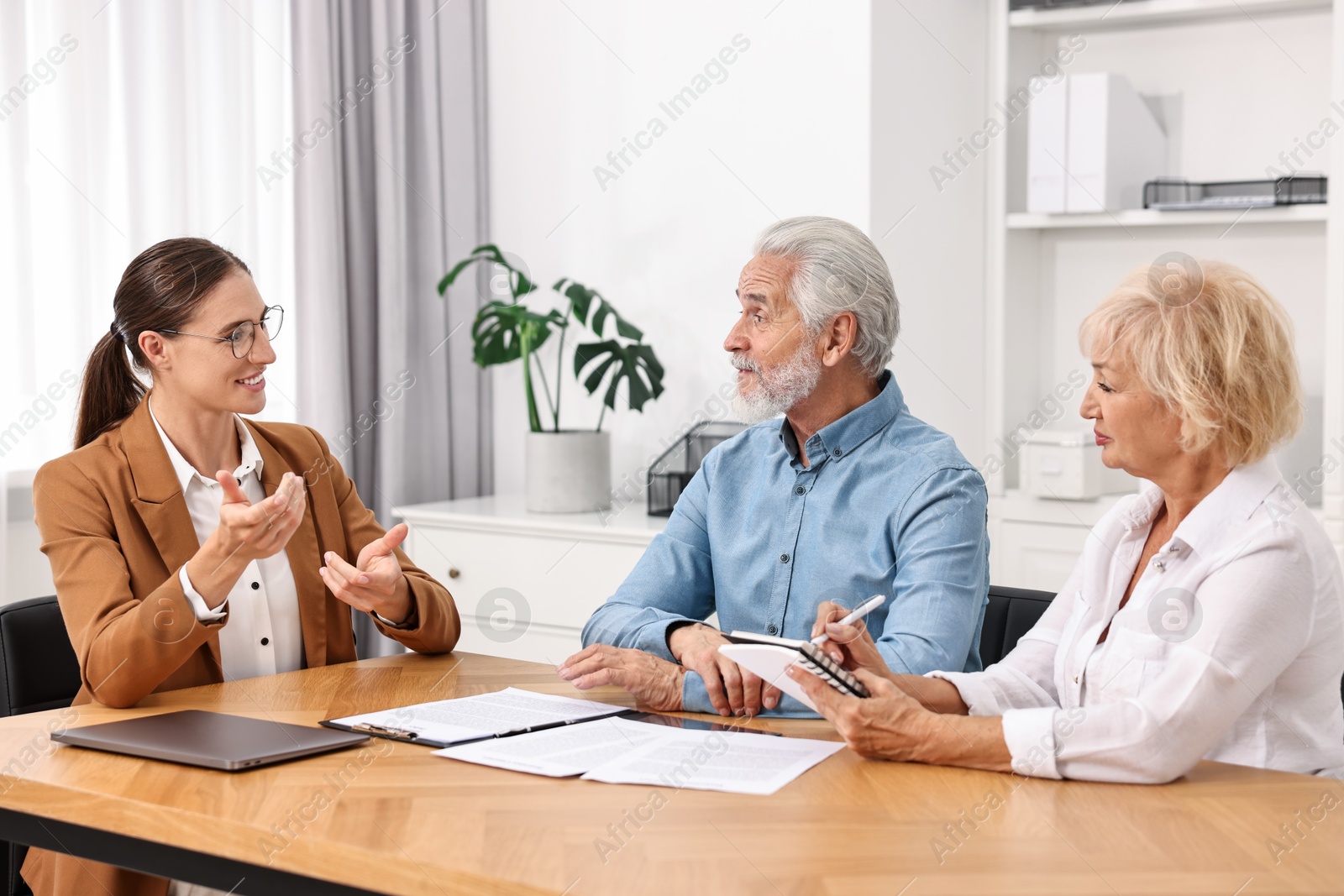 Photo of Pension plan. Senior couple consulting with insurance agent at wooden table indoors