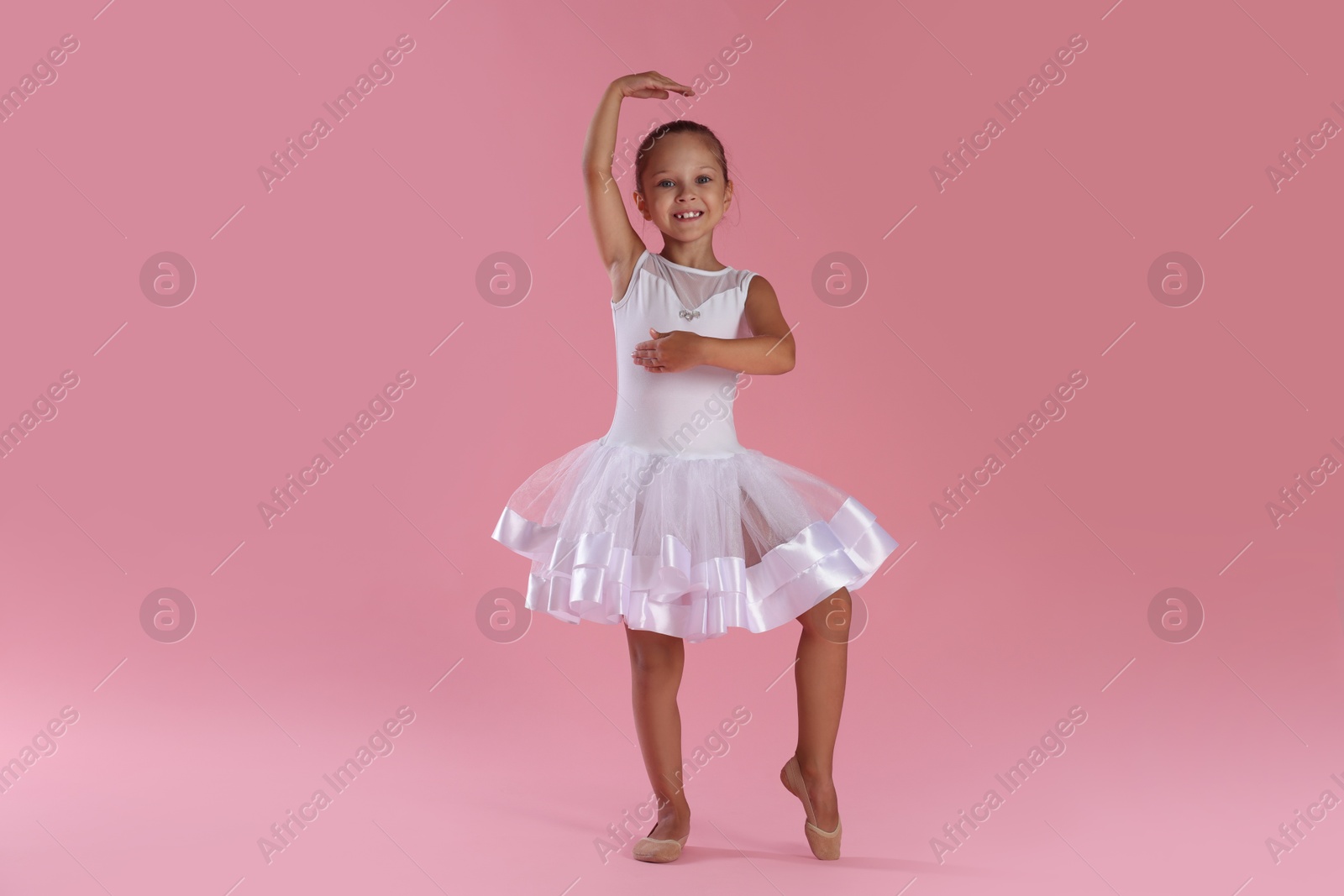 Photo of Little ballerina practicing dance moves on pink background