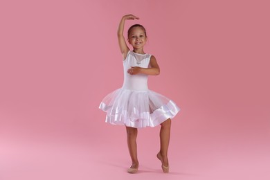 Little ballerina practicing dance moves on pink background