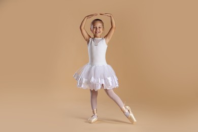 Photo of Little ballerina practicing dance moves on beige background