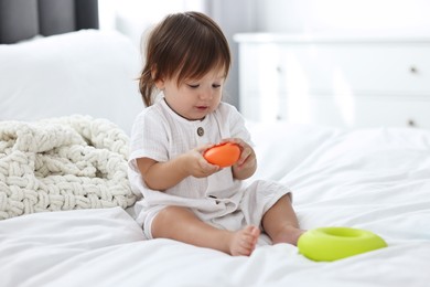 Cute little baby with toys on bed at home