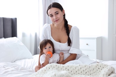 Photo of Beautiful young mother and her cute little baby with toy on bed at home