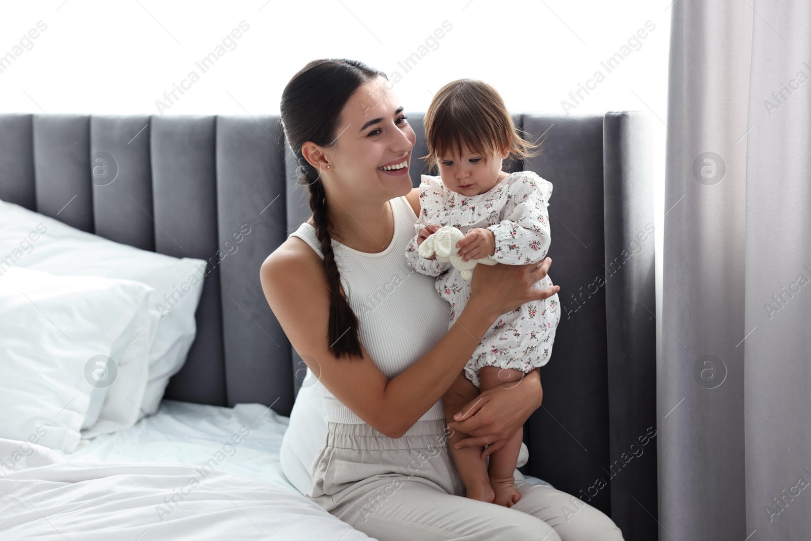 Photo of Beautiful young mother and her cute little baby with rabbit toy on bed at home